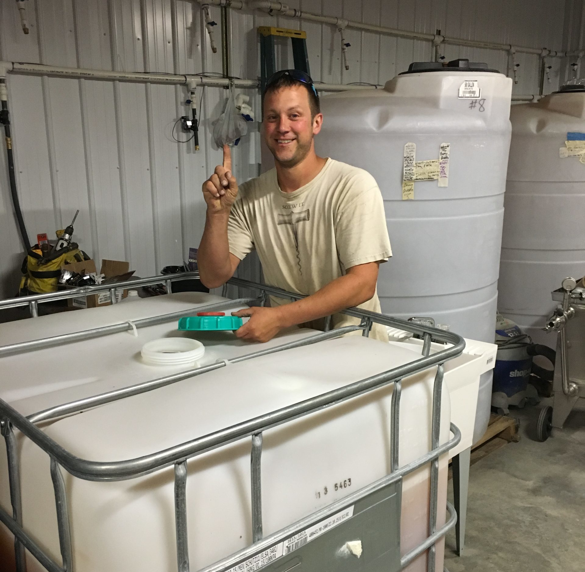 Peter standing in old production facility with a cube tank of wine.  Holding up his pointer finger to signify our first wine.