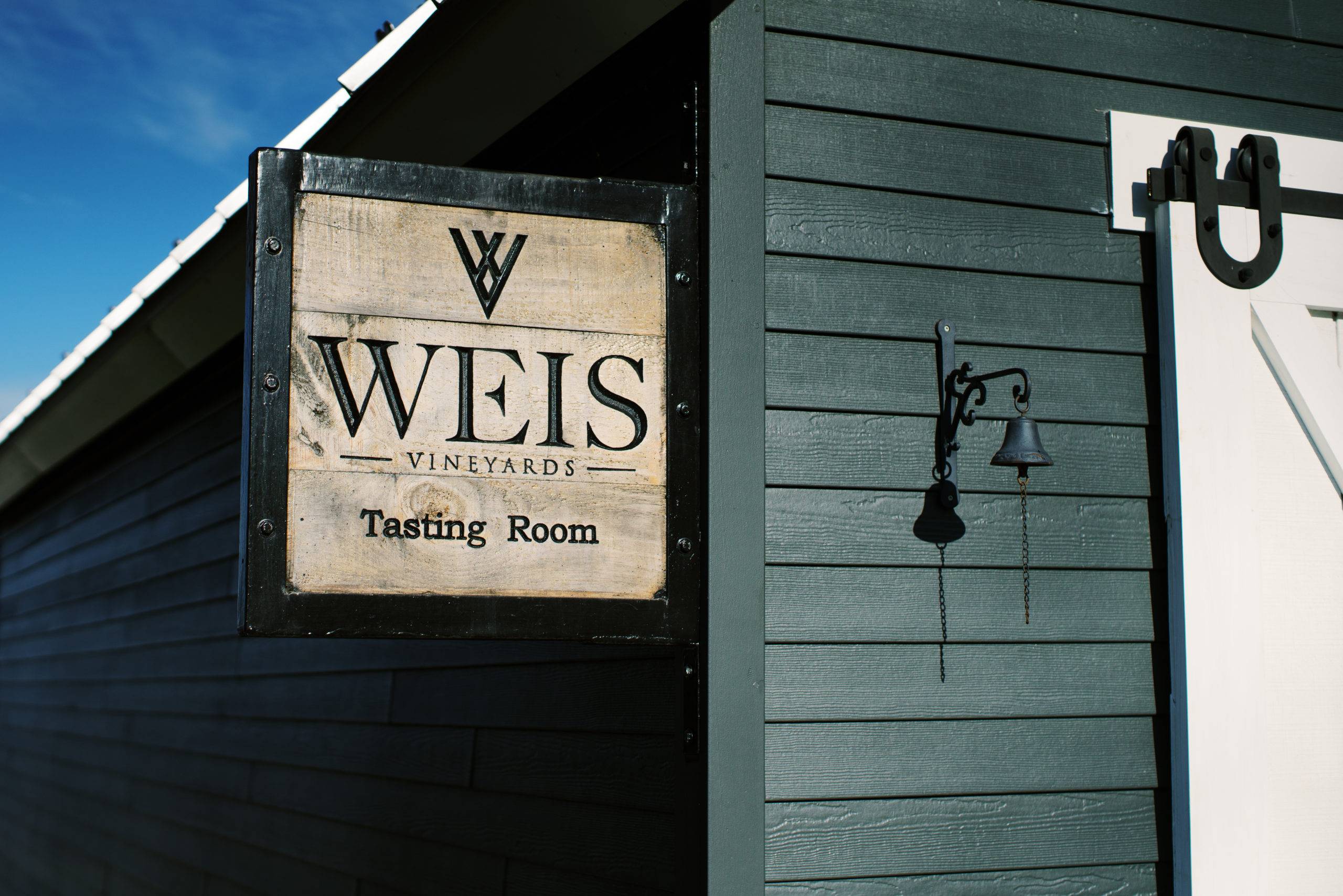 Front view of the tasting room schoolhouse.  Showcasing the new blue siding, white sliding barn doors, galvanized metal roof and small square sign on the side. 